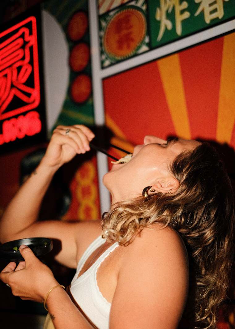 A guest dropping a dumpling into her mouth under the neon