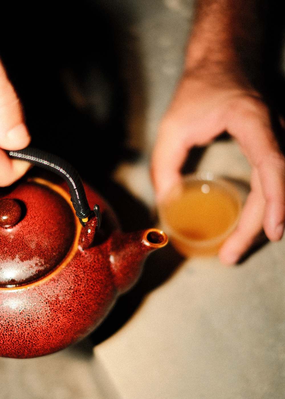 Pouring a cocktail from a speckled red teapot into a small glass